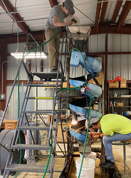 Trevor Gunn adding a sediment sample into the top hopper of the Humphrey spiral as David Hawkins splits the material at the bottom into lighter and denser mineral grain fractions
